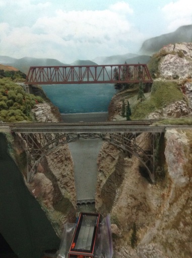 picture of model train bridges in front of a painted picture of a dam