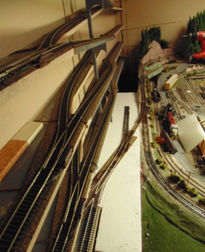 model railroad track running up a wall to the left and on to a table at the right