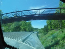 pedestrian bridge with top of rail car in foreground as seen from observation compartment of a following rail car